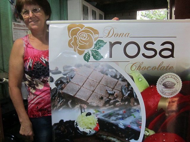 Rosalina Brighanti or Doña Rosa in her kitchen, where she makes jams and preserves, holding a sign advertising the organic chocolates made with the family’s special recipes, which are popular with consumers and businesses in Brazil and abroad. Credit: Mario Osava/IPS