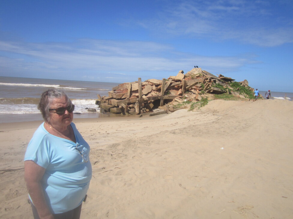 Sonia Ferreira, 79, president of SOS Atafona, stands next to what is left of the rubble of a four-story building, toppled by the sea in 2008. CREDIT: Mario Osava / IPS